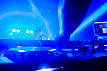 control DJ for mixing music with blurred people dancing at party in nightclub