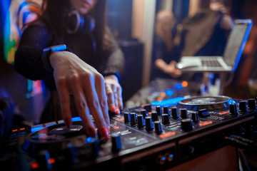 Blurred background with dj girl playing music and scratching tracks on professional dj midi...