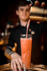 Bartender adding an alcoholic essence from a small glass bottle into the mixing glass on the bar counter