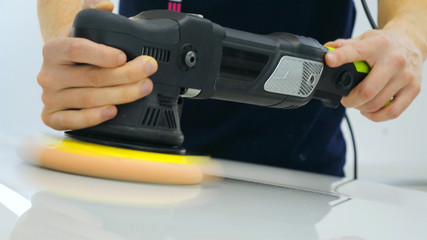 Closely shown as a professional worker polishes the transport (car) body using a polishing tool (machine). Concept from: Auto service, Car Painting, Machine washing.