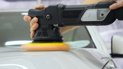 Closely shown as a professional worker polishes the transport (car) body using a polishing tool (machine). Concept from: Auto service, Car Painting, Machine washing.