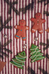 Gingerbread cookies with festive icing and Christmas tree twigs on red and white cotton background