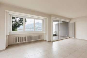 Empty room with radiators and large window overlooking Lake Lugano