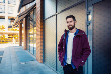 Fototapeta premium Half length portrait of handsome bearded man dressed in fashionable clothes standing on street.
