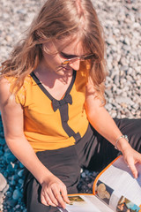 Attractive young blonde on the beach reading a magazine
