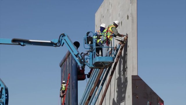 Men in a telehandler and ladder working in The Trump's Wall