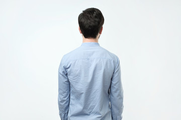 Young man in blue shirt standing alone back side view