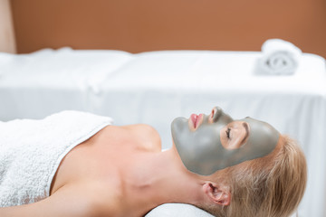 Obraz na płótnie Canvas Beautiful blonde woman lying with facial clay mask in spa