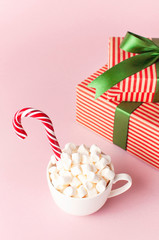 White mug with marshmallows Candy Cane gifts boxes with green ribbon on pink background Flat Lay Winter traditional drink food Festive decor. Christmas New Year presents Xmas holiday