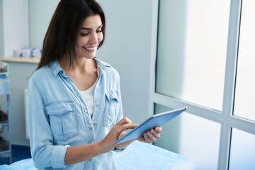 Waist up photo of happy woman filling out questionnaire while using tablet in beauty clinic. Copy...