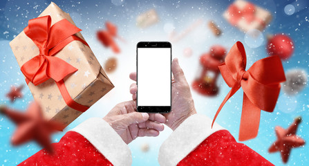 Santa's hands holding black phone with isolated screen on blue background surrounded with gift box, red ribbon and xmas tree ornaments. Mockup