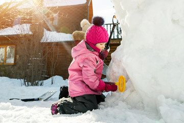 Children playing together in yard after snowfall in winter. Group of kids bilding figures and...