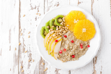 Sweet oatmeal porridge with pine nuts and fresh fruits - pear, orange, kiwi and pomegranate. Healthy dietary breakfast. Vegetarian dish