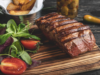 steak on the board with herbs, fried potatoes, spices on a black surface