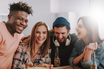 Spending time together. Portrait of multiracial young people sitting at the table with beer and snacks