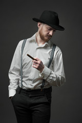 Side view of a stylish young man with suspenders smoking cigar