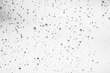 Dirty window glass with drops of rain. Atmospheric monochrome light background with raindrops. Droplets and stains close up. Detailed transparent texture in macro with copy space. Rainy weather.