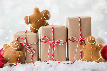Packing Christmas gifts.  Three Christmas gift boxes wrapped in kraft paper tied with red and white string and three smiling  gingerbread men cookies on white winter background. copy space - Powered by Adobe