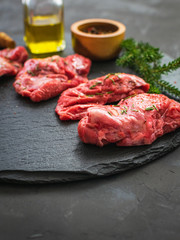 Raw pork cheeks meat on a dark gray surface with rosemary and spices. © Mila Bond