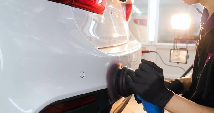 The professional guy (man) with headphones and a working uniform polishes the car body with a polishing tool. Concept from: Master class, Car Refreshment, Garage service, Special tools.