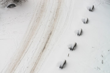 Snowy road. Fencing of old wheels. Fence from tires. Textured winter background. Abstract minimalist snowy weather texture. Car track in dirty snow. View from above. Traces of people and pets on snow.