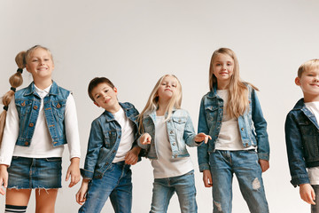 The portrait of cute little kids boy and girls in stylish jeans clothes looking at camera against white studio wall. Kids fashion and happy emotions concept