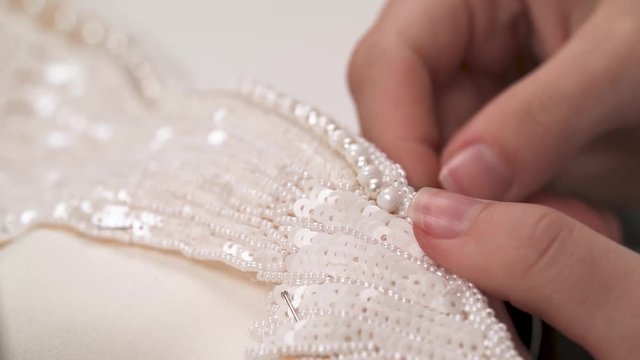 A dolly of woman's hands sewing beaded lace down the wedding dress