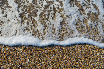 Seashore of shellstone with a coastal foamy wave