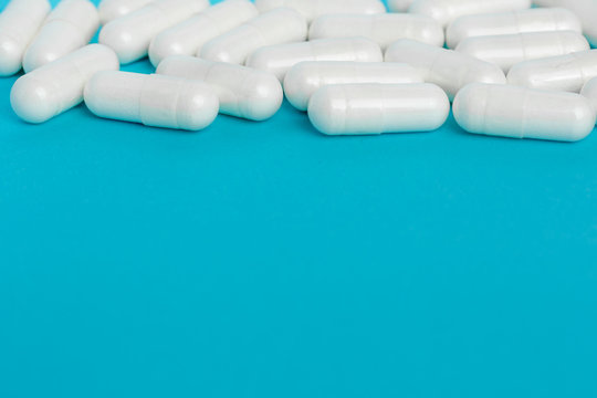 White capsules of medicine lie on a blue background.