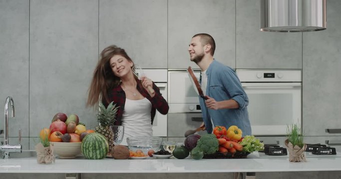 In the morning in a modern kitchen, couple have a good mood before starting to prepare breakfast they listen music and happy dacing and singing using kitchen hand mixer and a pan , spending a good