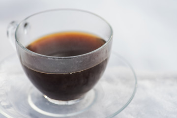 Winter holiday decoration concept: clear cup with coffee and saucer on frozen snow covered wood log in forest preserve park.