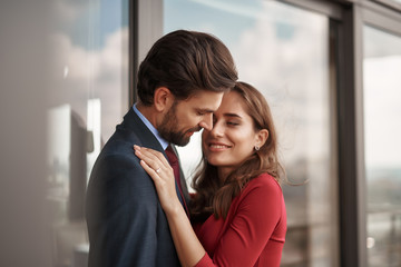 Concept of romantic engagement. Waist up portrait of happy beloved lady with golden ring on finger embracing with love to male lover while standing on balcony