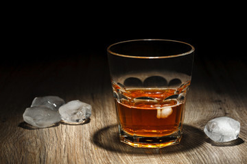 Glass of alcoholic drink with ice cubes on wooden table. Whiskey
