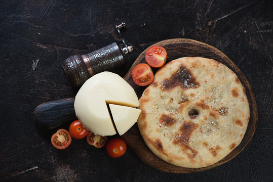 Ossetian pie with meat and suluguni cheese on a dark brown stone background, flatlay, horizontal shot