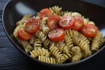 Close-up of fusilli pasta with green basil pesto and roasted tomatoes served in a black bowl, studio shot