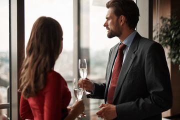 Concept of celebration. Waist up portrait of thoughtful couple with champagne glasses looking at city view from window of restaurant