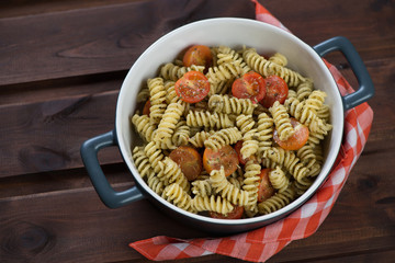 Italian fusilli with basil pesto sauce and roasted cherry tomatoes in a bowl, horizontal shot in a rustic wooden setting