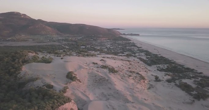 High aerial drone video orbiting left behind tall sand dune mountains view of Turkey's longest sand beach, ocean at sunset in Patara, Turkey. 4k at 23.97fps