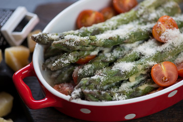 Closeup of baked asparagus with creamy garlic sauce, grated parmesan and cherry tomatoes, selective focus