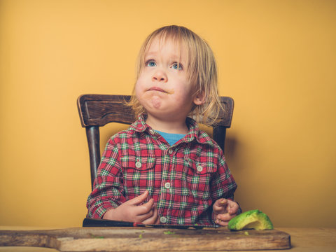 Little toddler cutting avocado at table