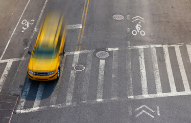 Overhead street view of yellow taxi cab speeding through an intersection crosswalk in New York City