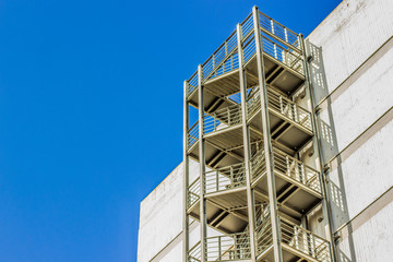 iron metal stairs construction for evacuation in exterior side of high apartment building on blue empty sky background, copy space