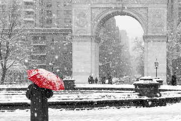 Person walking alone with red umbrella in black and white winter scene in Washington Square Park, New York City