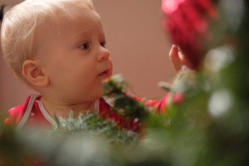 Little baby in red pajamas touches a christmas ball on a christmas tree