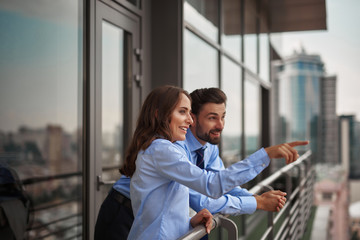Obraz premium Concept of friendly communication between coworkers. Waist up portrait of smiling woman showing something to man from office balcony while have work break