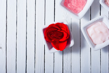 different cosmetic creams and bath salt with rose petals on white wood
