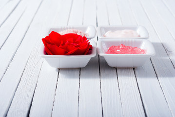 different cosmetic creams and bath salt with rose petals on white wood
