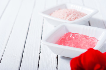 different cosmetic creams and bath salt with rose petals on white wood
