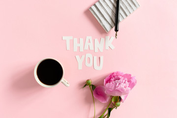 Quote Thank You made of letters cut out of paper. Peony, mug of coffee, notebook, calligraphy pen on a pink pastel background