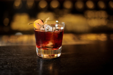 Glass of fresh and strong whiskey cocktail decorated with orange peel on bar
